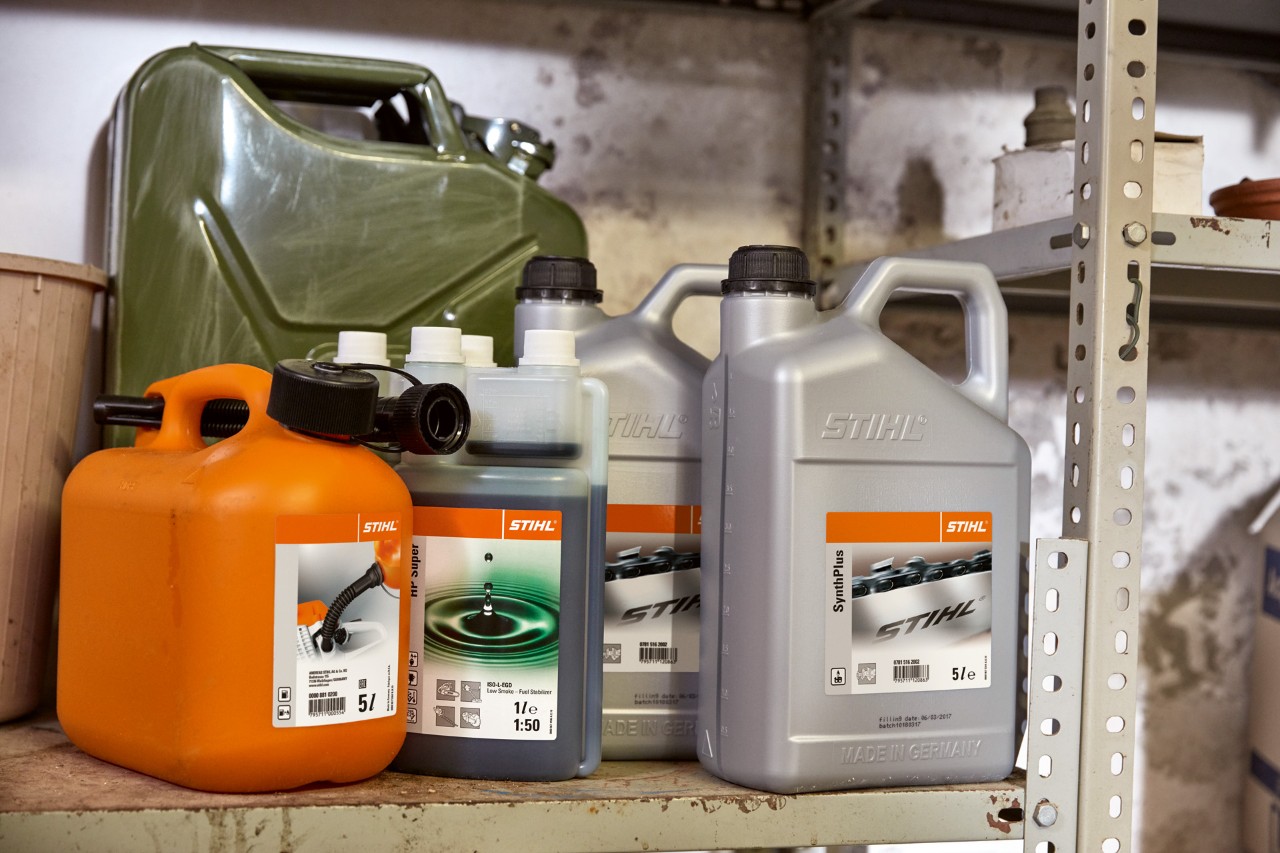 Recipientes com consumíveis STIHL numa garagem para reabastecer o corta-relva