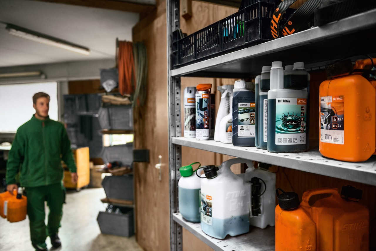 Um homem numa garagem com consumíveis STIHL para abastecer o corta-relva