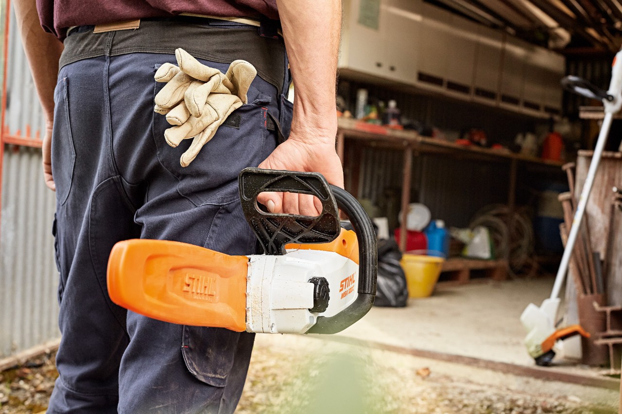 Um homem a encaminhar-se para uma oficina com uma motosserra a bateria STIHL com protetor de corrente