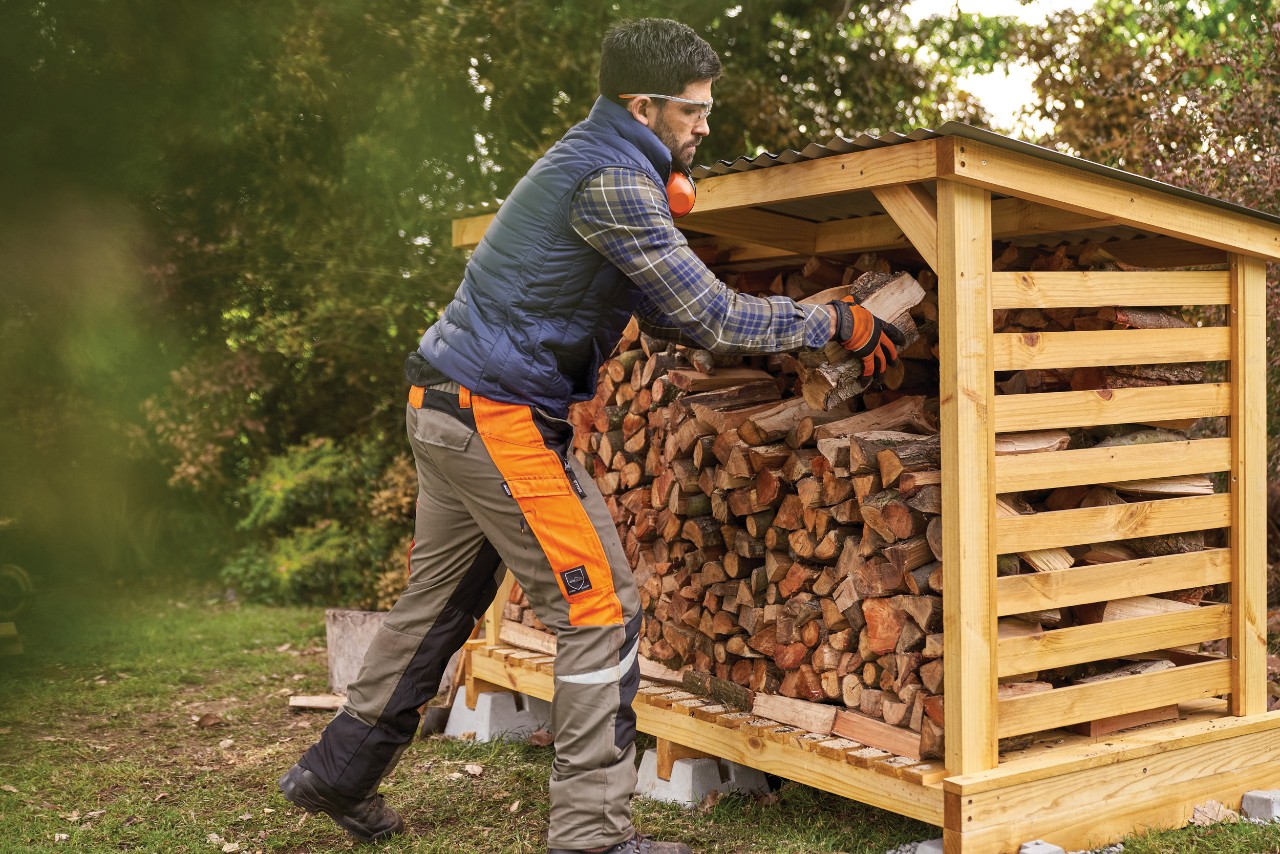 Um homem a empilhar lenha num lenheiro de bricolage