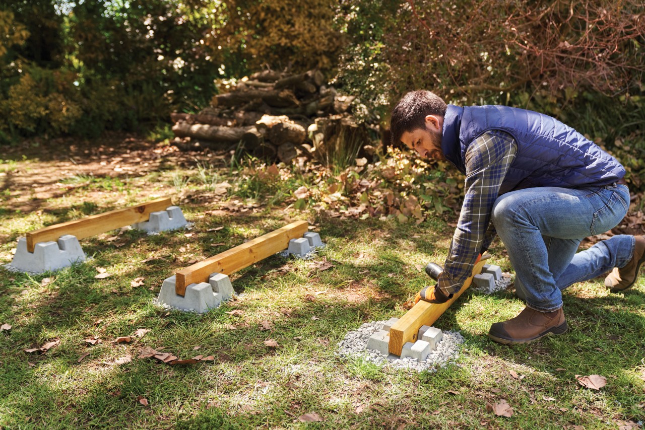 Como construir um lenheiro: um homem coloca três traves de madeira em fundações preparadas de sapatas para deck