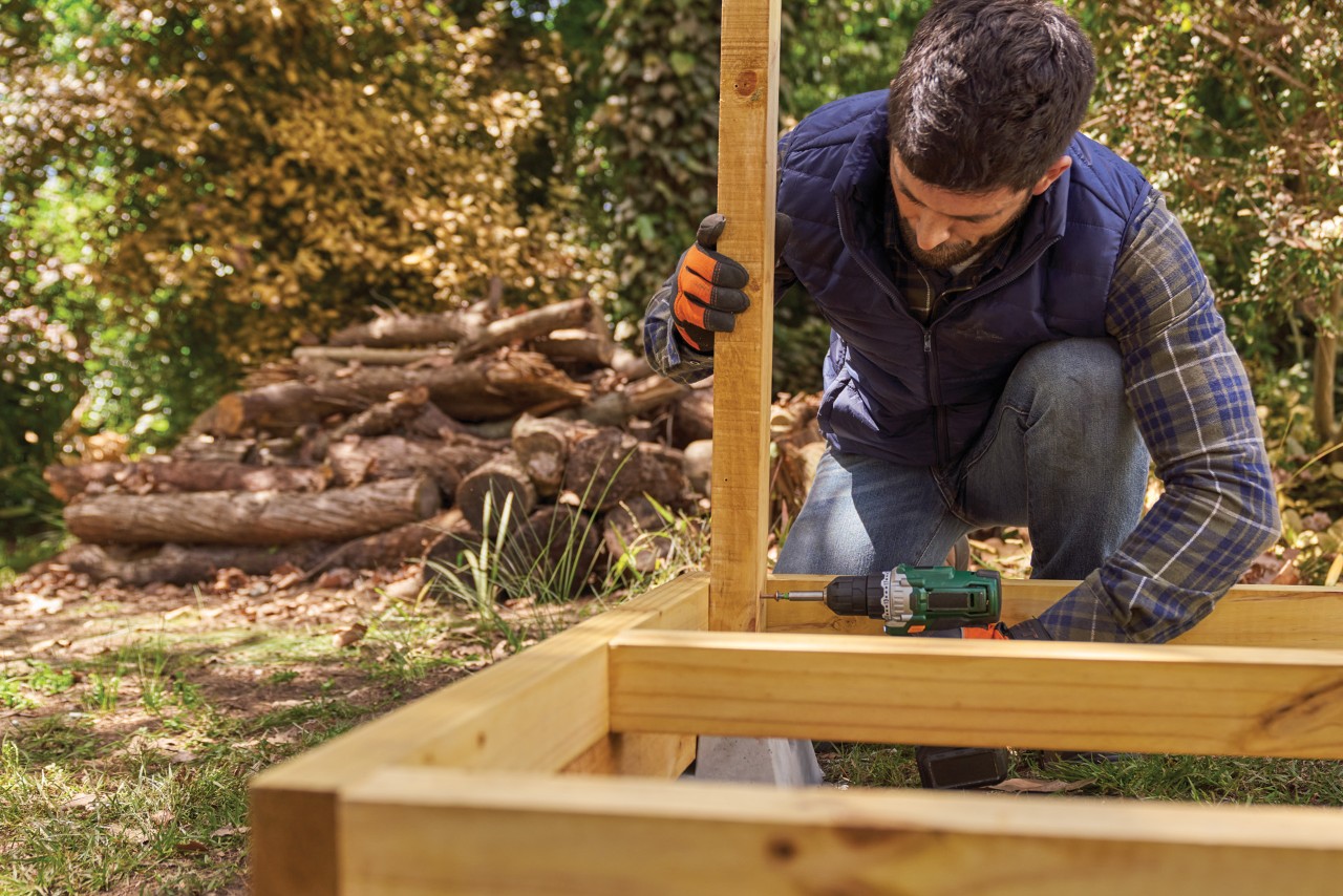 Como construir um lenheiro: um homem a fixar um pilar a uma estrutura de piso já construída