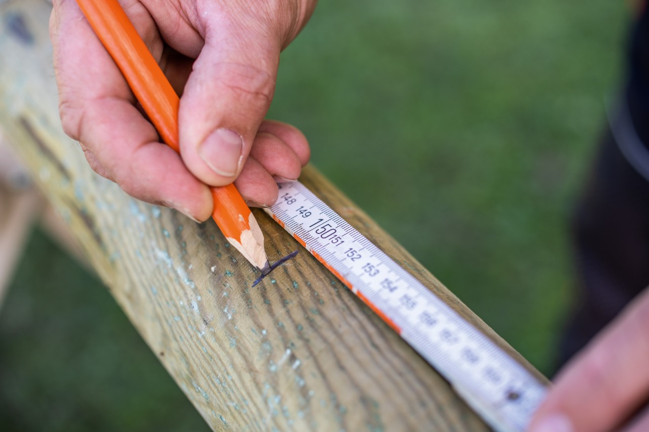A pencil and a carpenter’s rule is used to mark the length on the stakes.