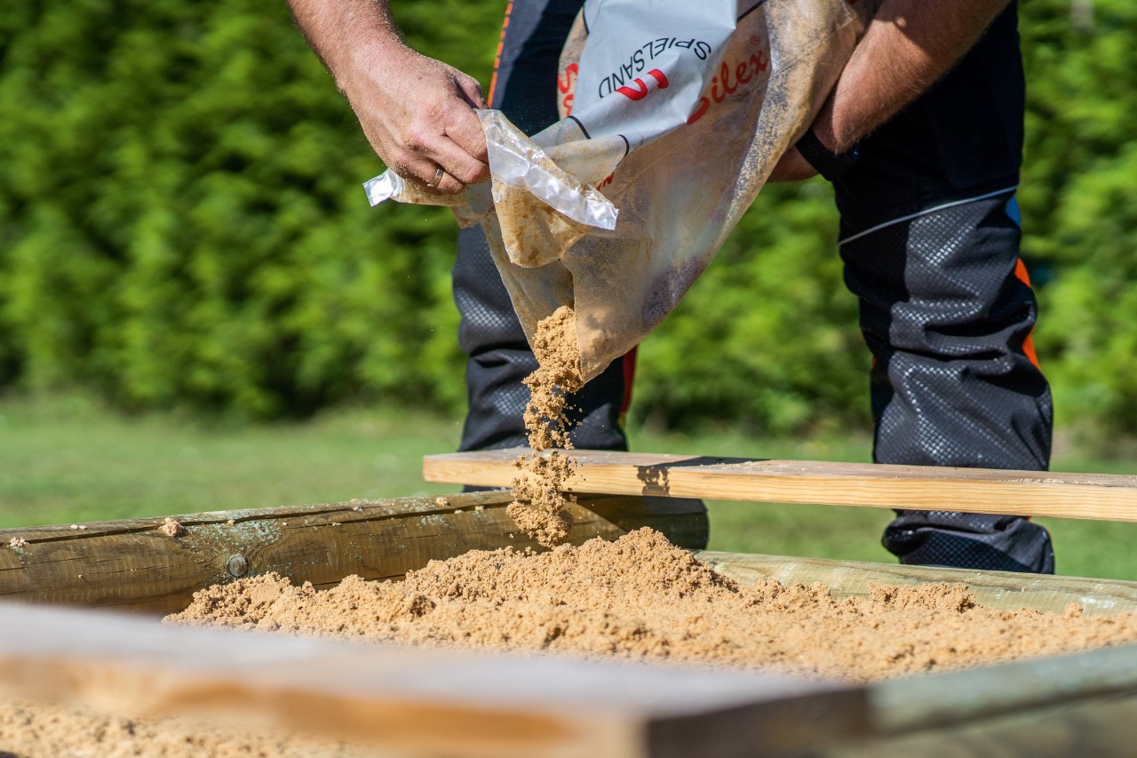 Uma caixa de areia de madeira a ser enchida com areia de um saco. Construção de caixa de areia infantil.