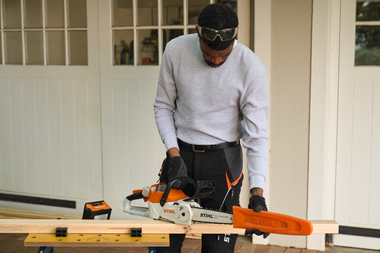 Um homem à frente de uma oficina remove a proteção de uma motosserra a bateria STIHL MSA 70 