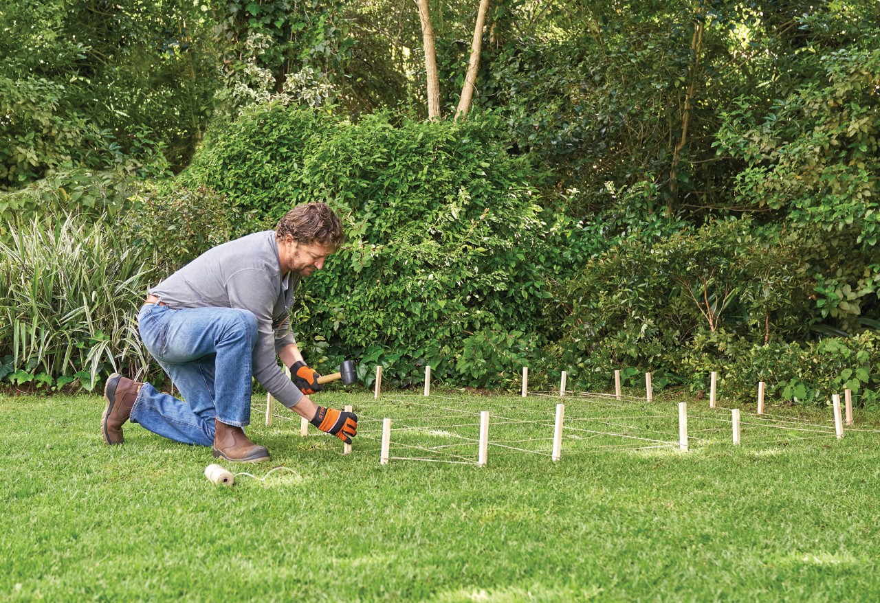 Como construir um abrigo de jardim: um homem a marcar com estacas o local para um abrigo na relva