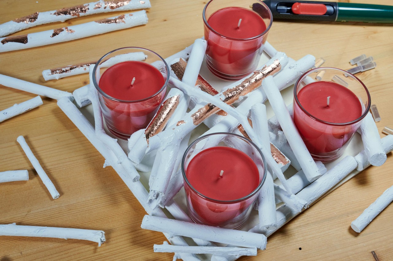 Centro de mesa de Natal de bricolage: galhos brancos a serem envolvidos à volta de suportes de velas na tábua.