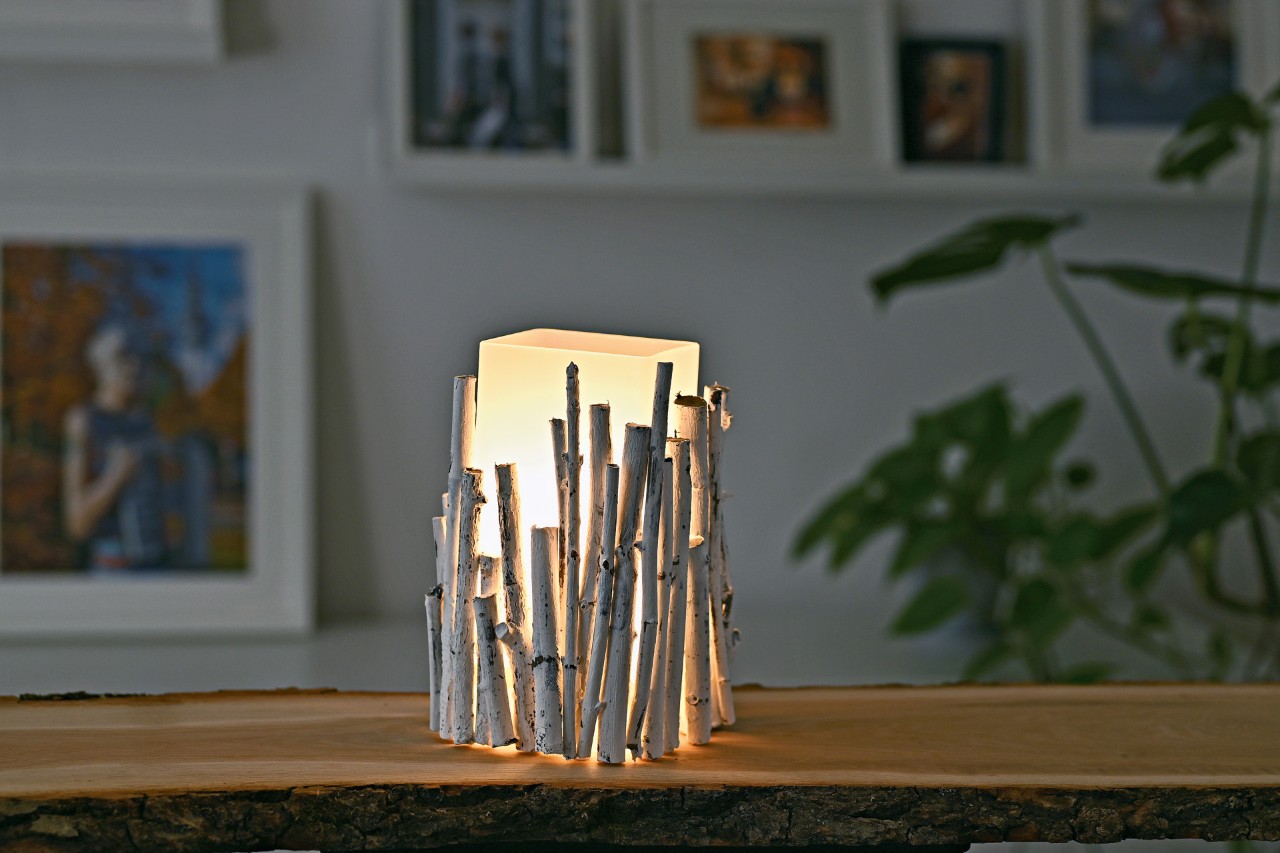 Luminária de mesa de bricolage com galhos: luminária acabada e acesa sobre uma mesa, com imagens numa parede de fundo 