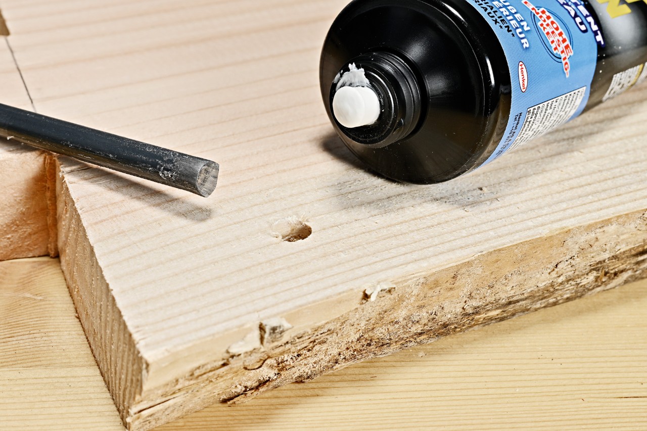 Mesa de apoio de bricolage: cola de construção e uma haste de metal ao lado de um furo aberto na tábua de madeira