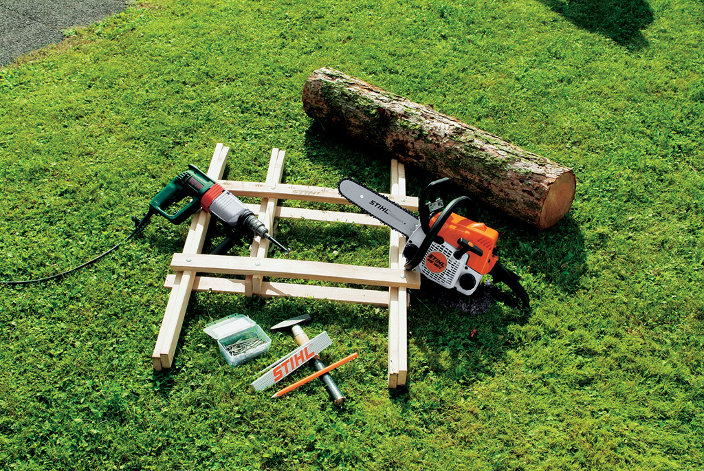 Pedaço de tronco, motosserra STIHL MS 180 C, metro desdobrável, martelo, u cavalete e um berbequim sobre relva verde