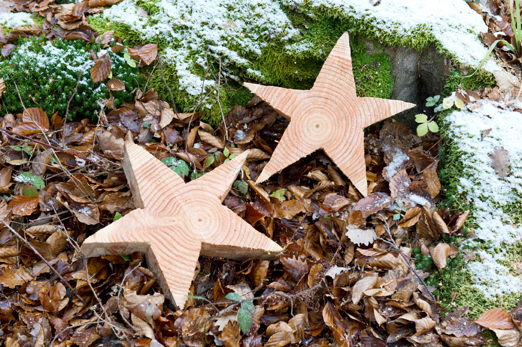 Fazer uma estrela de madeira: duas estrelas de madeira sobre folhas e musgo coberto de neve