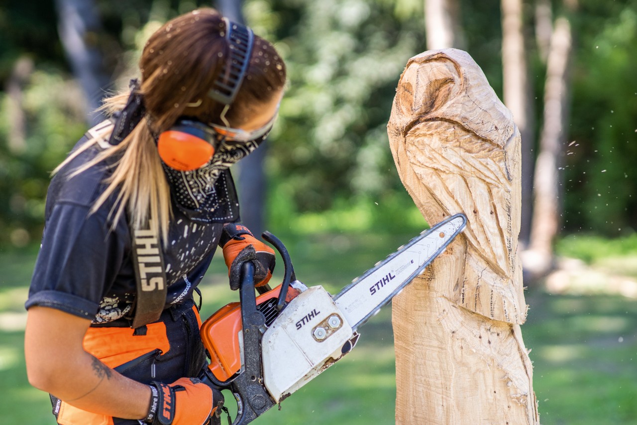 Mulher a esculpir uma coruje com a motosserra e a dar detalhe às penas de voo com um kit de escultura.