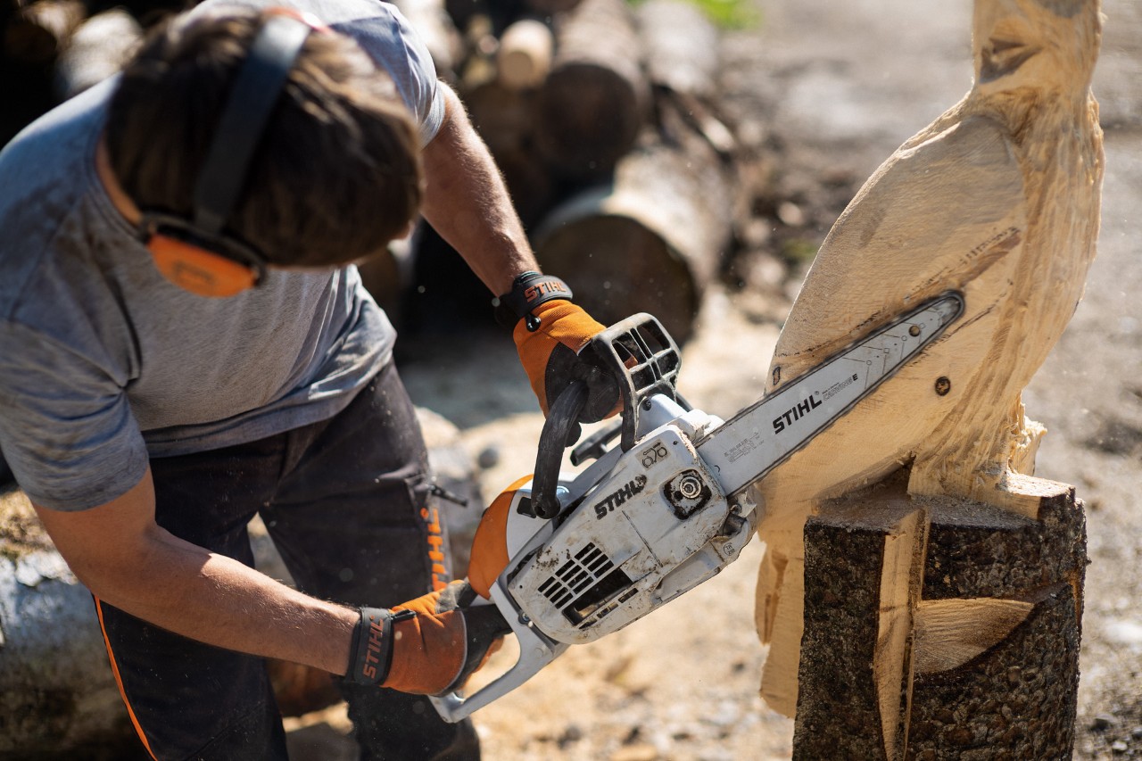Um homem a usar uma motosserra STIHL MSE 193 CE para esculpir as asas numa ave de madeira – escultura com motossera
