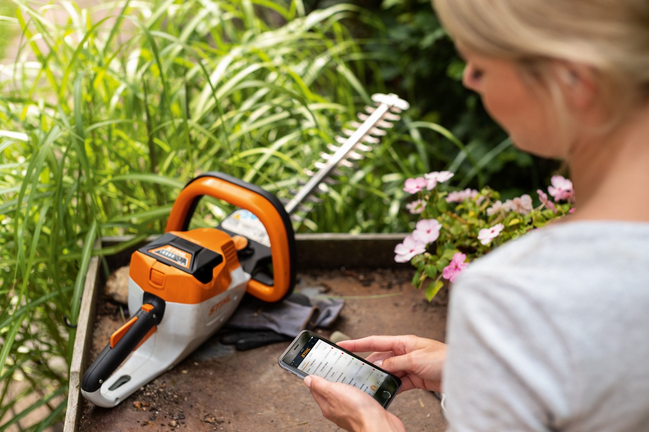 Uma mulher a registar a sua podadora de sebes a bateria STIHL HSA 56 com o seu smartphone
