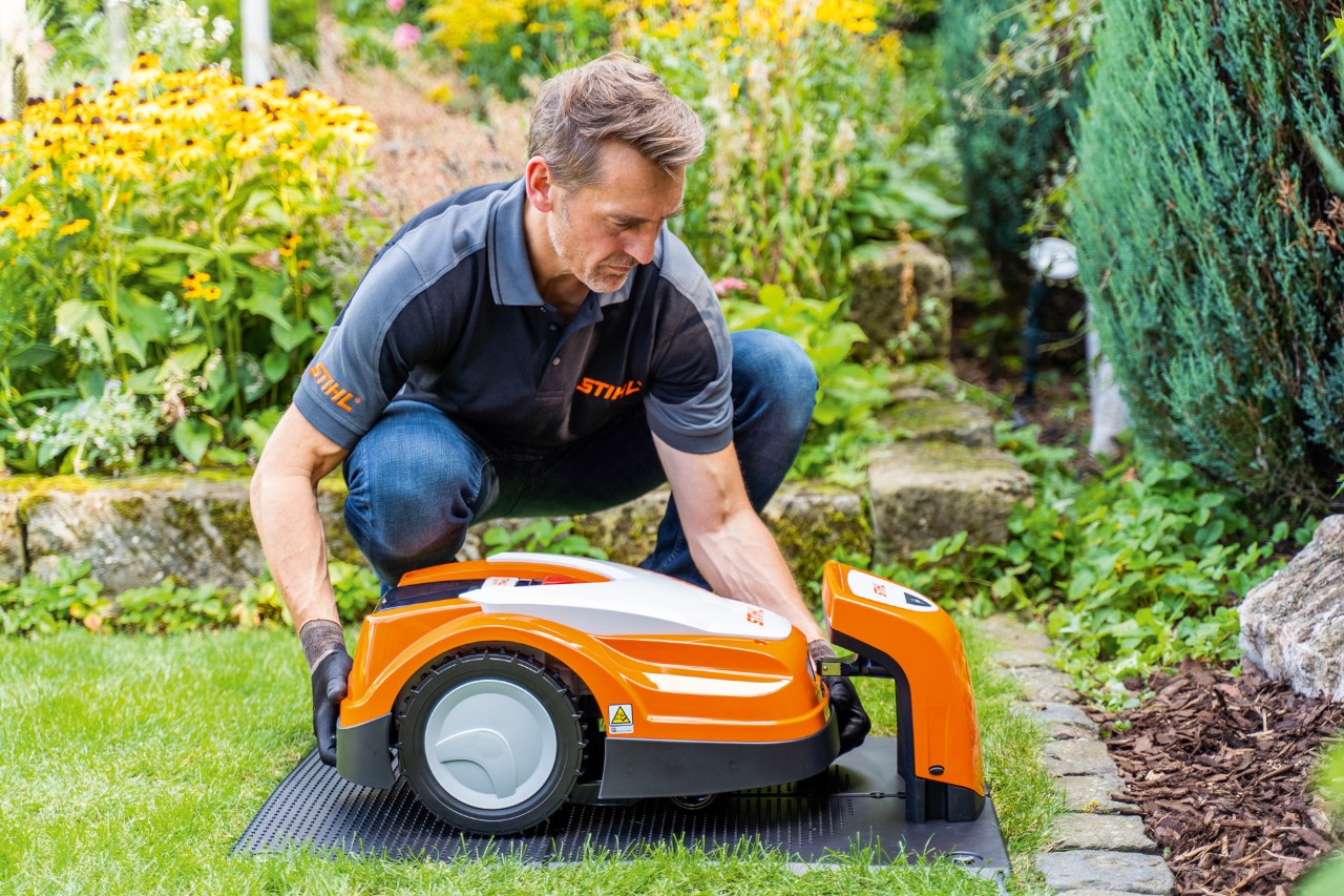 Um concessionário STIHL coloca um robot corta-relva STIHL iMOW no carregador num jardim