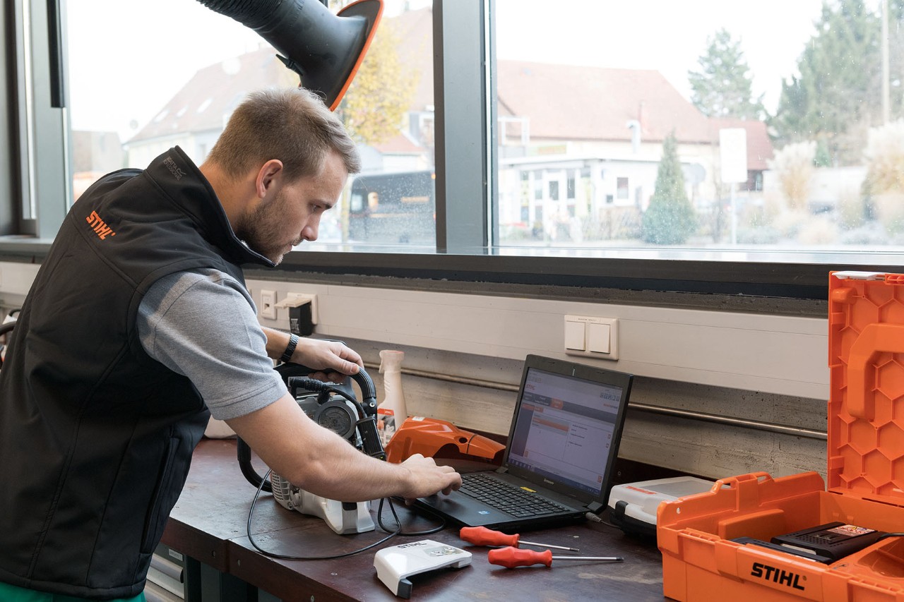 Homem a olhar para um computador portátil numa oficina. Ao lado, uma motosserra STIHL.