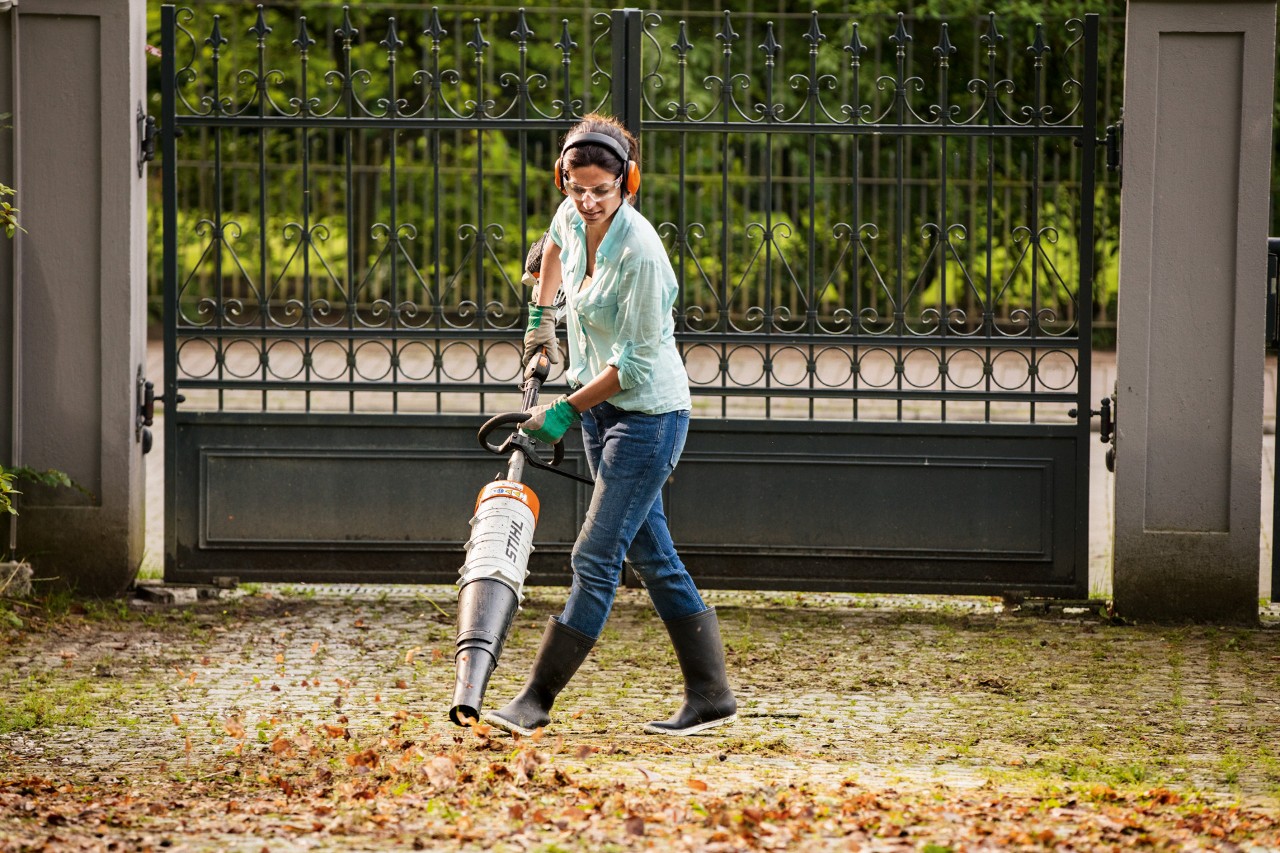 Mulher com óculos de segurança e proteção auditiva a usar um STIHL KM 131 R KombiEngine acoplado a um soprador de folhas