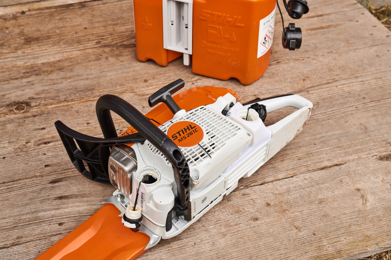 Uma motosserra MS 261 a gasolina no chão, com tampa de depósito da STIHL e o reservatório do óleo removidas.