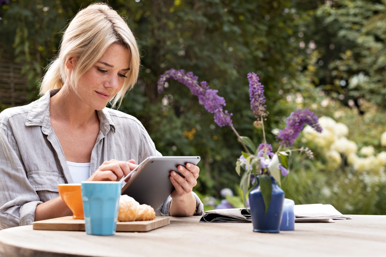 Uma mulher a usar um tablet sentada a uma mesa ao ar livre