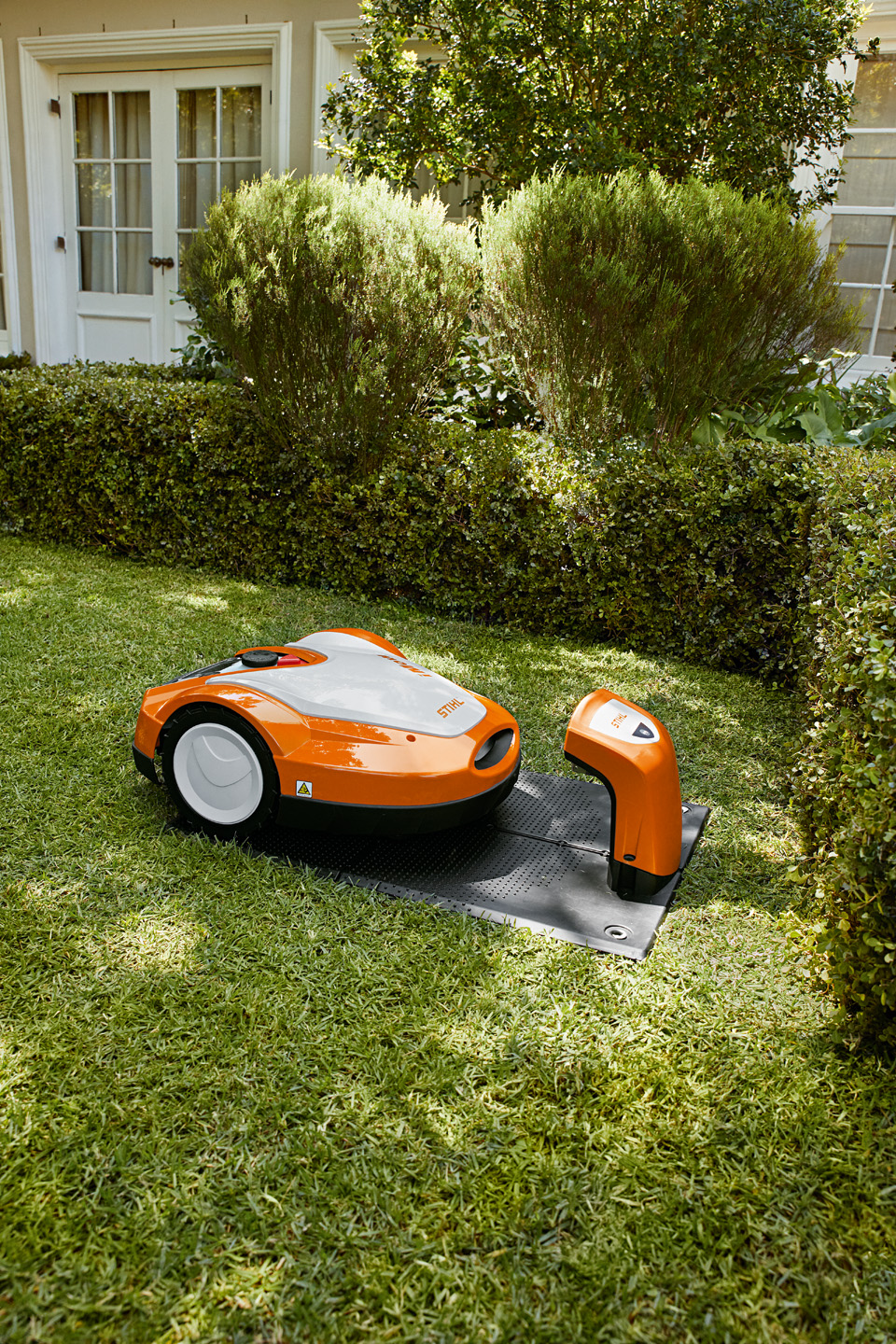 Um robot corta-relva STIHL iMOW® RMI 632 na estação de carga num jardim.